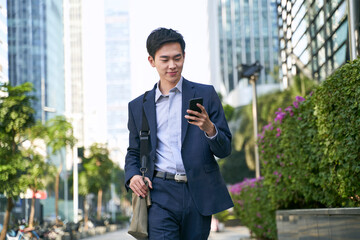 young asian business man looking at cellphone while walking in the street