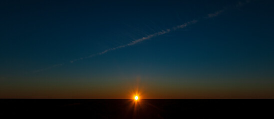 Fototapeta na wymiar Setting sun on a clouldless evening with a vapour trail in the Australian outback