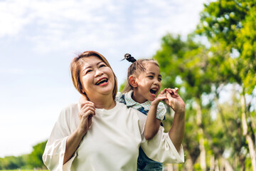 Fototapeta premium Portrait of happy love asian grandmother and little asian cute girl enjoy relax in summer park.Young girl with their laughing grandparent smiling together.Family and togetherness