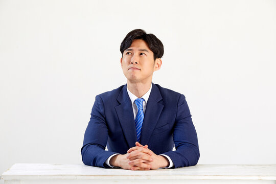 흰 배경 앞에 정장 입은 고민하는 30대 한국 남자