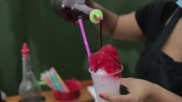 joven vendedor sirviendo un vaso de helado con zumo de fresa llamado "cold cold" , bebida fr&iacute;a