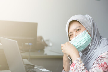 Muslim woman wearing a mask working using a laptop in the office in new normal style. Work at home concept.