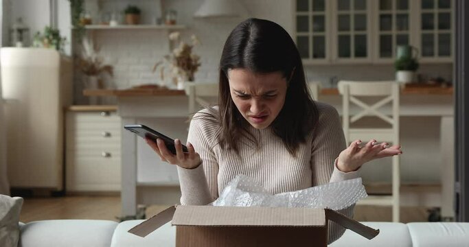 Unhappy young woman unboxing parcel, checking internet order in mobile shopping app, dissatisfied with received wrong crashed item, stressed client having negative experience, purchasing goods online.