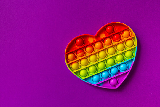 Pop it fidget toy on purple background with copy space. Rainbow heart anti stress fidget. Valentines day concept and first love concept