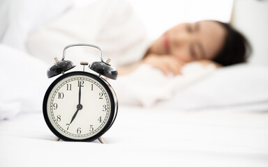 Young asian woman happy sleep at morning in bedroom. Closeup of alarm clock on white bed