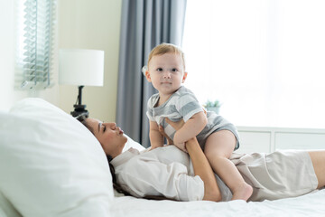 Caucasian loving mom play with cute baby boy child on bed in bedroom