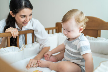 Obraz na płótnie Canvas Caucasian mom read storytale to baby infant in child crib in bedroom. 