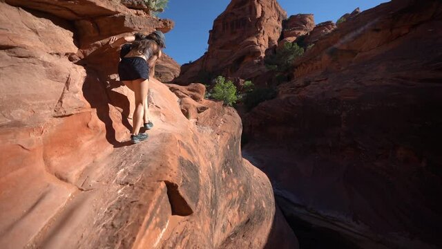 Back of Young Female HIker Walking on Steep Red Rock Sandstone Cliff. Hiking Trails in St. George Region, Utah USA
