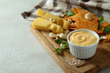 Board with cheese sauce and snacks on white textured table