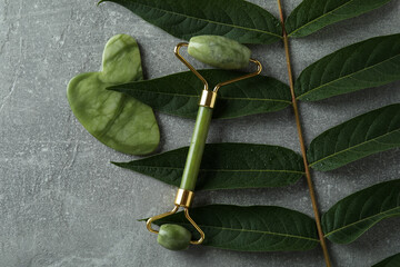 Face roller, gua sha and twig on gray textured background