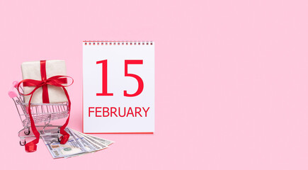 A gift box in a shopping trolley, dollars and a calendar with the date of 15 february on a pink...