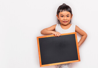 Asian Little child girl holding a small blank black board with smiling face. Back to school concept. Wall background. Wearing white tank top. Looking at camera.