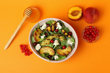 Plate of salad with grilled peach on orange background
