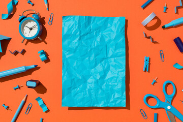 Top view photo of vivid blue crumpled paper sheet and school accessories blue stationery on isolated orange background with copyspace