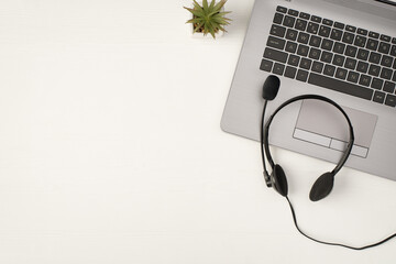 Top view photo of black wired headset on grey laptop and plant on isolated white wooden table...
