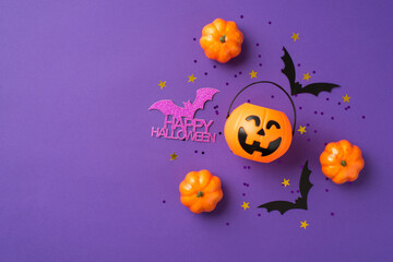 Top view photo of halloween decorations pumpkins basket black sequins golden stars bat silhouettes and purple inscription happy halloween on isolated violet background with copyspace