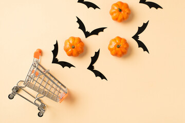 Top view photo of shopping cart model with flying bats silhouettes and small orange pumpkins on...