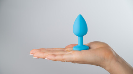 Woman holding a blue butt plug on a white background. Adult toy for alternative sex
