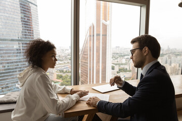 African client applicant communicates with employer advisor during formal meeting in office boardroom, city with modern skyscrapers view through panoramic window. Negotiations, job interview concept