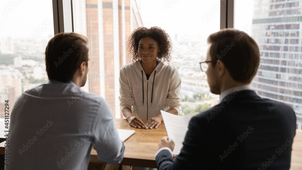 Poster Rear back view two HR male managers interviewing African ethnicity female vacancy applicant. Passing of job interview at formal meeting in office boardroom, headhunting agency work, staffing concept