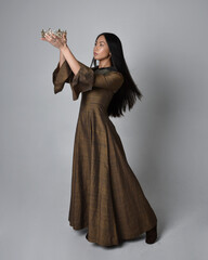 Full length  portrait of beautiful young asian woman with long hair wearing medieval fantasy gown and golden crown. Graceful standing pose,  isolated on studio background.