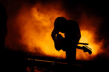 Silhouette of a guitar player in the smoke. The guitarist plays at a rock concert.