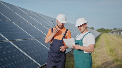 Coworking engineers on solar plant. Adult men in hardhats, An employee of a power plant transmits...