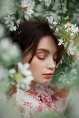 Woman with natural makeup, floral cosmetics for skin of the face, girl posing in flower branches of blooming apple tree in spring
