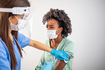 Doctor applying a vaccine on a woman's arm. Closeup of a nervous woman and her doctor wearing face...