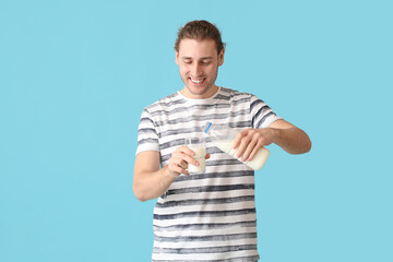 Young man pouring milk in glass on color background