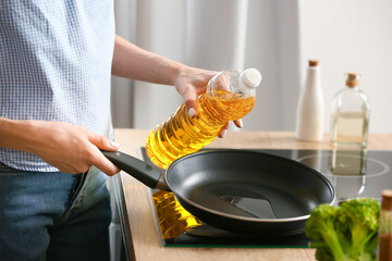 Young woman pouring oil into frying pan in kitchen - obrazy, fototapety, plakaty