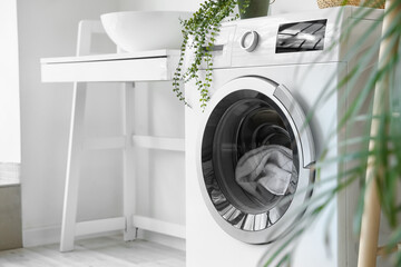 Modern washing machine with laundry in bathroom