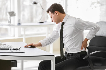 Young man suffering from back pain in office