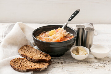 Bowl with tasty sauerkraut soup, sour cream and slices of fresh bread on light wooden background