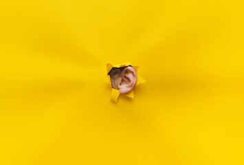 Fototapeta Close-up of a woman's ear through a torn hole in yellow paper. The concept of eavesdropping, espionage, gossip, tabloids and the yellow press. Background with copy space. obraz