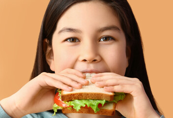 Little girl eating tasty sandwich on color background, closeup