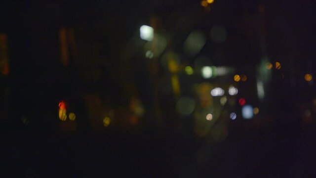 Looking through broken glass revealing blurred, dark and scary city lights background at night time.