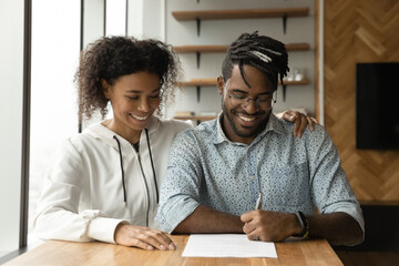 Happy millennial African couple make deal signing rent contract or loan documents sit in modern...