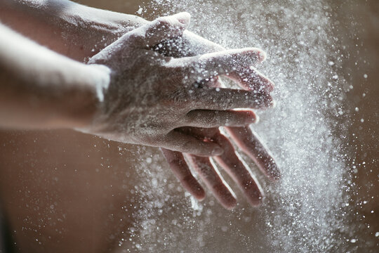 Girl shaking hands off flour, close-up photo of hands in backlight, blurred background