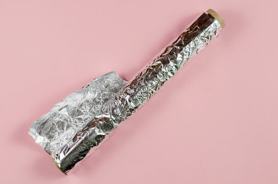 Crumpled foil opposite the pink background. Roll of aluminum foi