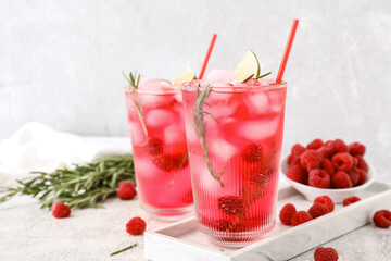 Glasses of tasty raspberry lemonade and berries on light background