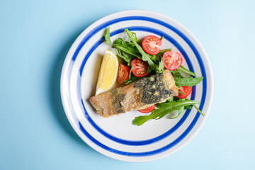 Delicious battered fish on a plate with cherry tomatoes, arugula and a piece of lemon.