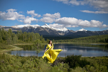 beautiful girl, brunette in a yellow dress walks near a mountain lake