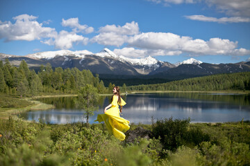 beautiful girl, brunette in a yellow dress walks near a mountain lake