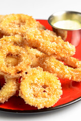 Golden onion rings and sauce in a saucepan served on a red plate. Over white background.