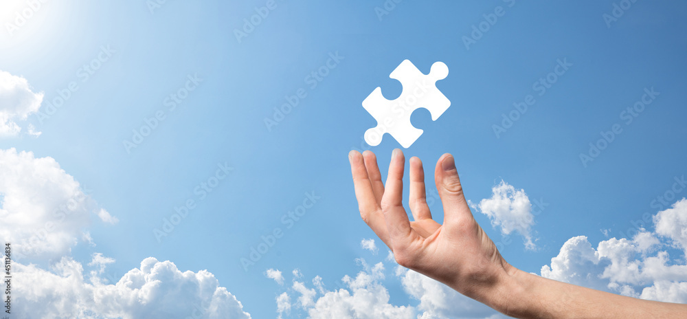 Wall mural Male hand holding puzzle icon on blue background. pieces representing the merging of two companies or joint venture, partnership, Mergers and acquisition concept.