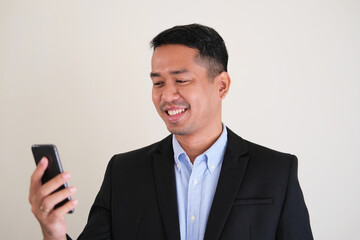 Asian man wearing black suit smiling happy while looking to his mobile phone