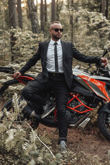 Fototapeta na wymiar Cool man and black red colored motorbike in forest