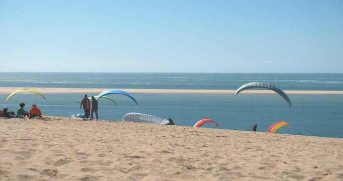 A group of people on the shore of the beach preparing to practice paraglading, with parachutes of beautiful and colorful colors