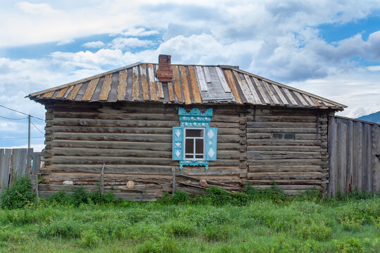 Old Russian log house with window and carved shutters. Chimney on roof. Horizontal image.